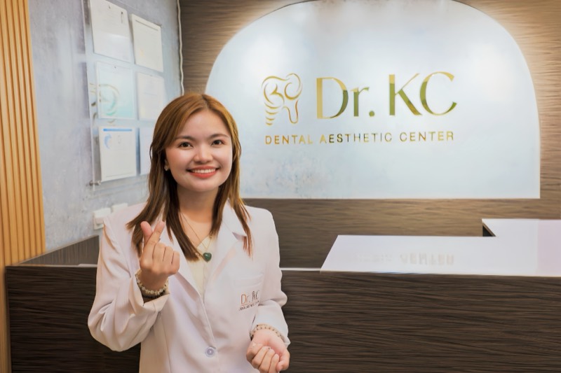 Dr. KC Robles in a white coat, smiling at the reception desk of Dr. KC Dental Aesthetic Center in Makati City